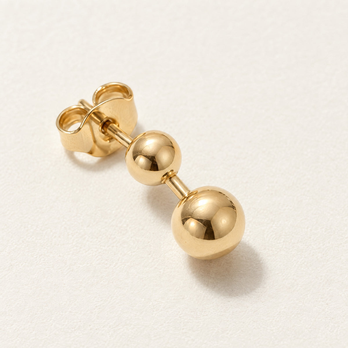 Close-up of an Echo Studs earring: two polished gold spheres joined by a short bar, with the post and butterfly back