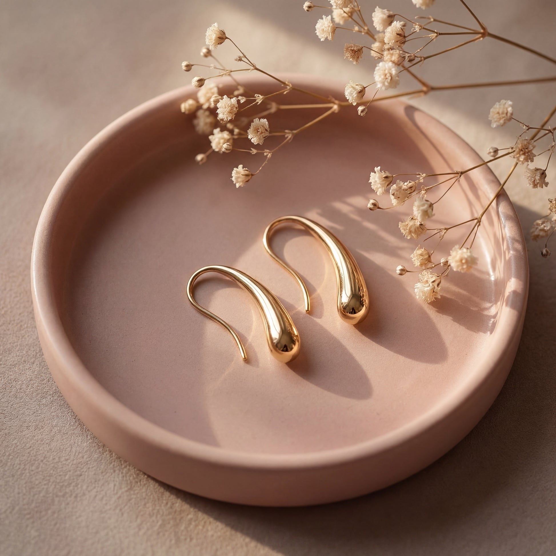Gold earrings on a pink ceramic dish with dried flowers