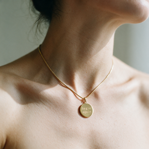 Origin Disc necklace worn on the neck, a fine gold chain with a round pendant engraved begin again