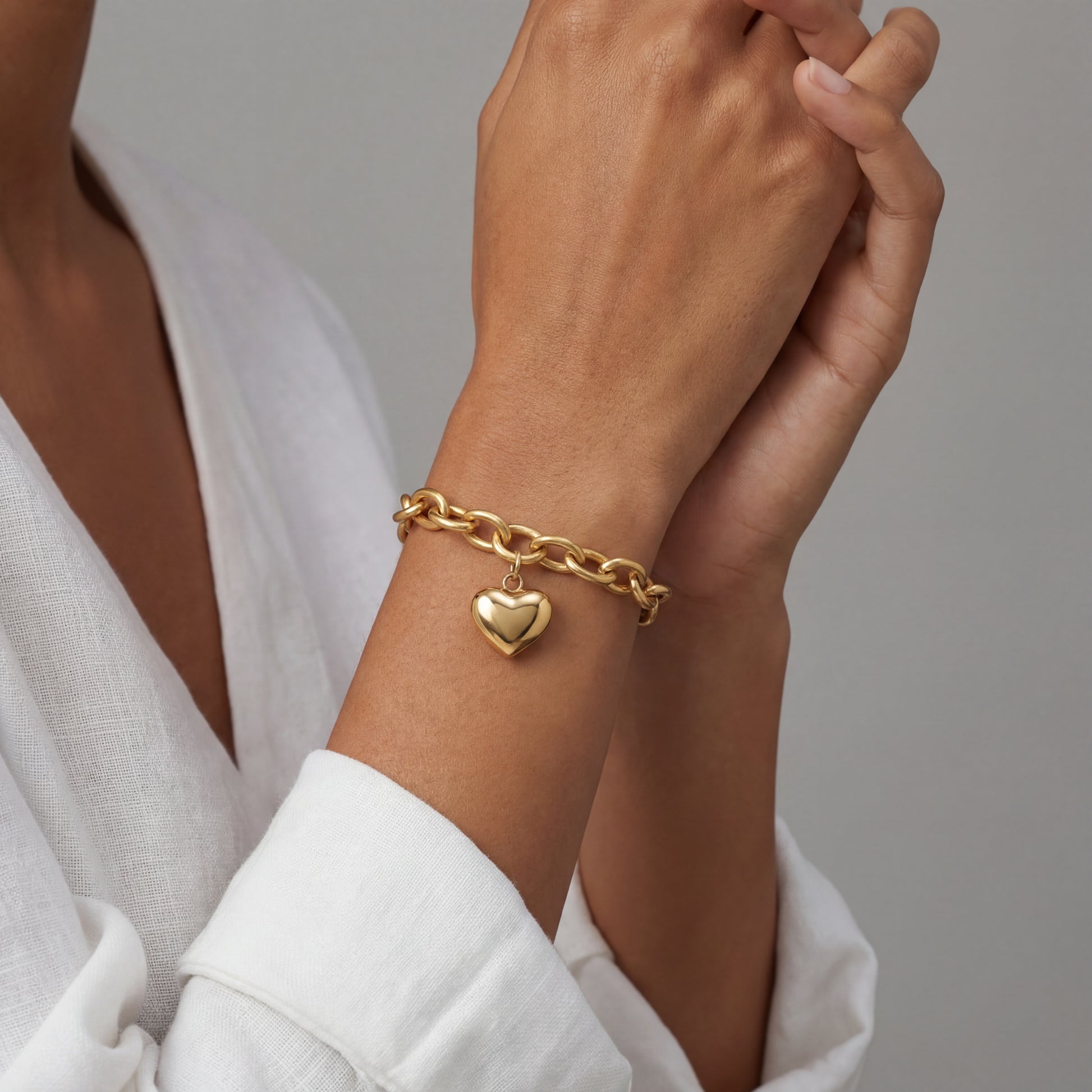 Woman wearing 14K gold plated chunky chain bracelet with puff heart charm on wrist over white linen, hypoallergenic gold bracelet