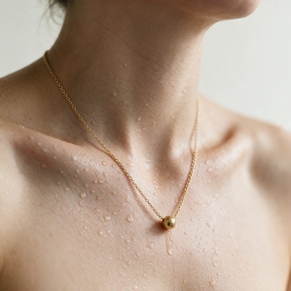 Whisper Chain necklace with a small gold bead on a fine 14K gold chain, worn on skin with water droplets