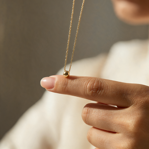 Whisper Chain necklace held between two fingers, showing the small gold bead on a fine 14K gold chain